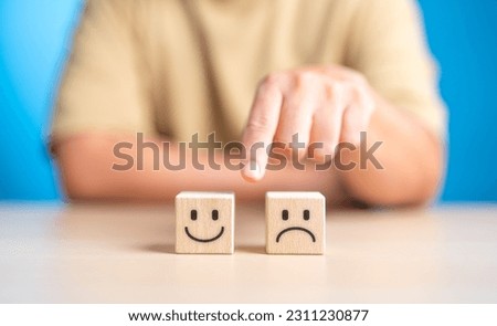 Hand making a decision between two wooden cubes with happy and sad face for positive or negative mindset selection. Emotional state and mental health concept. Like or Dislike for client satisfaction. Royalty-Free Stock Photo #2311230877