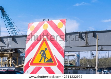 A road sign warns of approaching a section of road where repairs are being carried out. Road signs at the bridge construction site. Metal span of the bridge. Safety on the road.