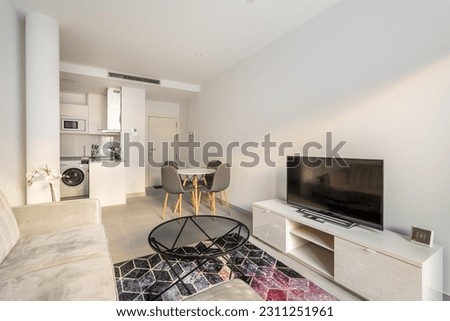 Studio apartment with a combined kitchen and living room with a corner sofa, tables and chairs and a TV with a picture on the background of a kitchen set and a hallway