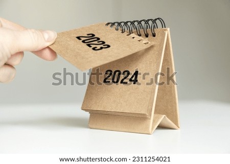 a woman's hand turns over a calendar sheet. year change from 2023 to 2024. Royalty-Free Stock Photo #2311254021