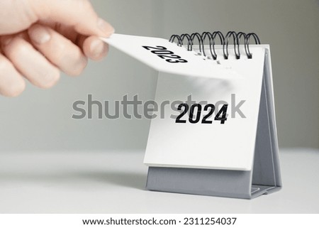 a woman's hand turns over a calendar sheet. year change from 2023 to 2024 Royalty-Free Stock Photo #2311254037