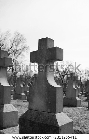 Simple and plain stone cross designating a grave in the local Christian cemetery in a black and white monochrome.
