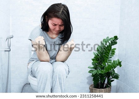 chronic constipation concept with Asian woman sitting in the toilet having the lumpy and difficult passage of hard stools and bowel movements  Royalty-Free Stock Photo #2311258441