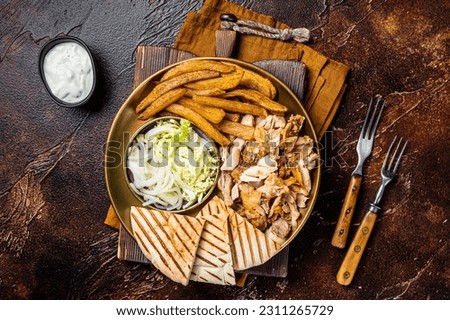 Turkish Doner kebab or gyros on a plate with french fries, vegetables and salad. Dark background. Top view.