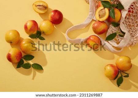 Top view of fresh ripe peaches (prunus persica) with green leaves on the stem are dropped from the mesh bag and spread on the yellow background. Blank space for text and design Royalty-Free Stock Photo #2311269887