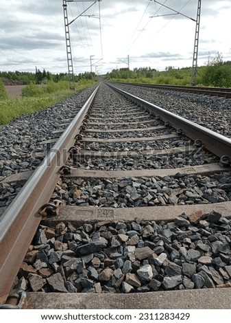Picture of a railway track continuing towards the horizon. Cloudy sky on the background.