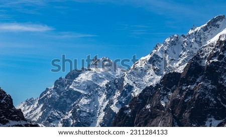 Snow-covered rocky brown mountain peaks of the mighty Himalayas amid the clear blue sky. A beautiful view of a glacier on the mountain slope and a lonely planet with a serene environment.
