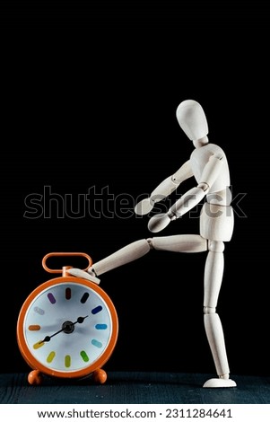 A human wooden dummy foot on a table clock, isolated on black