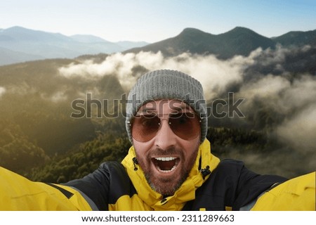 Smiling man in hat and sunglasses taking selfie in mountains