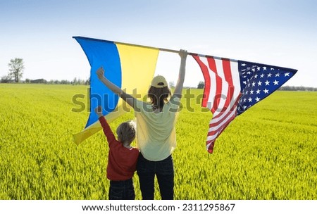 unrecognizable woman with child on sunny day stands with back and raises two large flags - American and Ukrainian. concept of cooperation and friendship. US aid to Ukraine to win the war with Russia