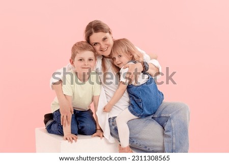 A young mother has fun playing with a cute little daughter and son, holding in her arms, gently hugging on a pink background