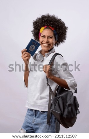Brazilian passport. Young black woman with black power curly hair, white t-shirt, smiling and holding a Brazilian passport. Isolated on white background.
