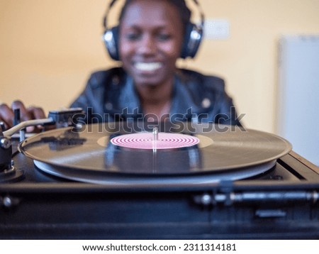 young woman wearing a leather jacket using headphones while playing a vinyl record on a vintage turntable