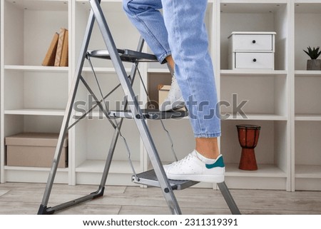 Young woman on stepladder near bookshelf at home, closeup Royalty-Free Stock Photo #2311319391