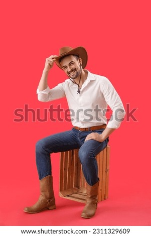 Handsome cowboy sitting on red background