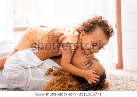 Happy family parent and child spending time together on holiday vacation. Mother playing and hugging little daughter on the floor in living room at home. Parenting and family relationship concept.