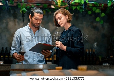 Professional man and woman sommelier tasting and smelling red wine in wine glass at wine cellar with wooden barrel at wine factory. Alcohol liquor shop, brewery, winery industry and winemaker concept. Royalty-Free Stock Photo #2311335773