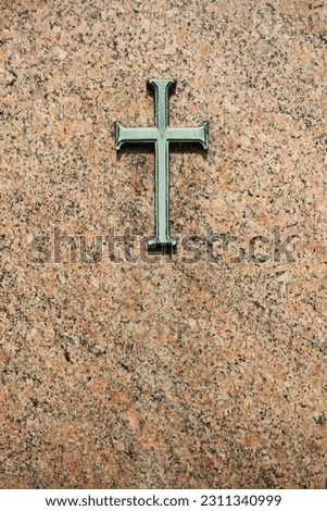 A copper cross with green patina hanging on a granite rock wall.