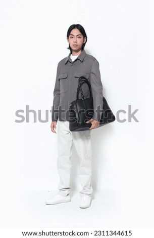 Full body portrait of handsome male  wearing jacket holding handbag   posing on white background