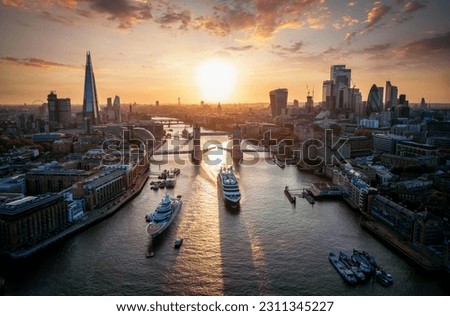 Panoramic aerial view of the skyline of London, England, with a passenger ship crossing under the Tower Bridge during a beautiful sunset