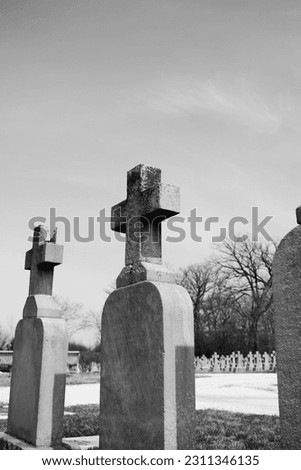 Simple and plain stone cross designating a grave in the local Christian cemetery in a black and white monochrome.