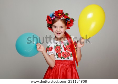 Studio image of a happy cute little girl in the Ukrainian national costume holding a yellow and blue air balloon on a gray background on Holiday