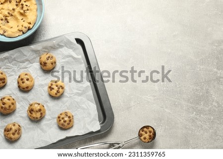 Bowl with dough and uncooked chocolate chip cookies on light grey table, flat lay. Space for text