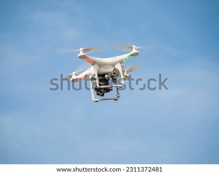A white drone with an attached action camera is flying in the blue sky.