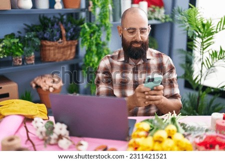 Young bald man florist using smartphone and laptop at flower shop