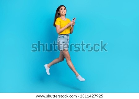 Full size portrait of charming energetic girl jumping use smart phone blogging isolated on blue color background
