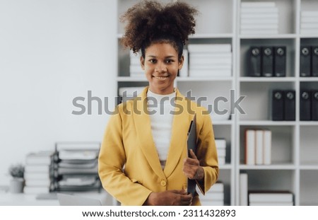 Young confident businesswoman with arms crossed smiling looking at camera in office