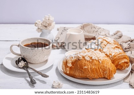 Good morning concept. Breakfast with cup of coffee and fresh croissant. Sweet creamy sauce, hard light, dark shadow. White wooden background, copy space