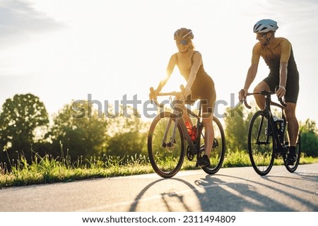 Portrait of a couple of athletes dressed in activewear biking on paved road. Countryside area, sunny day outdoors. Professional road bicycle racers in action while riding outside of the city.