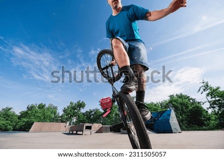 Cut off picture of a skilled tattooed urban man practicing freestyle tricks on his bmx in a skate park. Cropped picture of a cool middle-aged man balancing on one wheel on his bike.