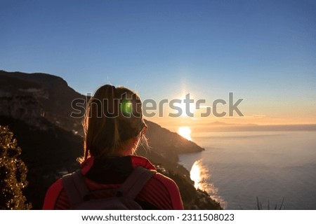 Active woman with backpack watching sunrise from hiking trail Path of Gods between Positano and Praiano, Amalfi Coast, Campania, Italy, Europe. Calm water surface reflecting sun ray, Mediterranean Sea Royalty-Free Stock Photo #2311508023
