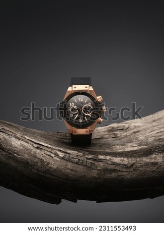 Beautiful gold men's watch with a black strap on a wooden stand, on a gray background. Beautiful gold watch. A luxury brand watch.  Royalty-Free Stock Photo #2311553493