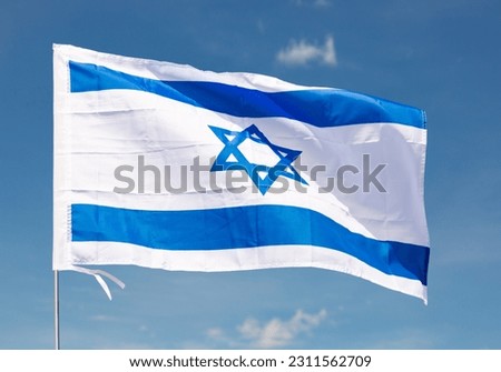 Large flag of Israel fixed on metal stick waving against background of clear sky during daytime Royalty-Free Stock Photo #2311562709