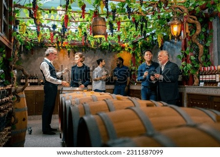 Professional sommelier explaining and recommending wine tasting to group of customers and visitors at wine shop or liquor store. Winery liquor manufacturing industry and winemaker business concept. Royalty-Free Stock Photo #2311587099