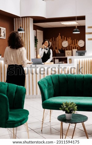 Hotel manager verifying files in lobby lounge area at reception counter, checking registration forms and booking details. Young adult ensuring to provide modern service for guests. Royalty-Free Stock Photo #2311594175