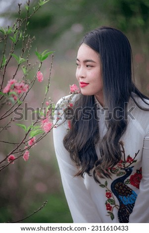 Beautiful Vietnamese girl wearing ao dai taking pictures with plants, flowers, customs and traditions of the Lunar New Year in Vietnam.
