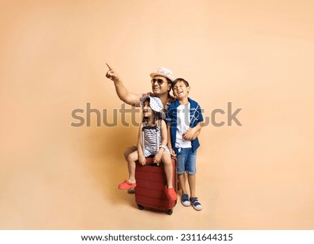 Young Indian father with his kids going for summer vacations isolated over beige background, Father with his kids and trolley luggage bag go for Holidays and travel, copy space. Royalty-Free Stock Photo #2311644315