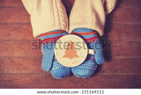 Hands in mittens holding hot cup of coffee. Photo in old color image style.