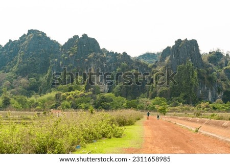 Dirt path with green fields and luxurious mountain in the background, Thakhek loop, Laos.
