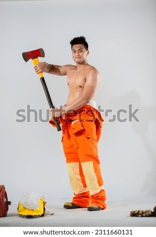 Attractive firefighter standing topless holding an iron axe while looking the camera with happy expression.