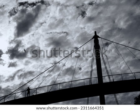 Monochrome image of a modern curved bridge in Sassnitz on the island of Ruegen on which the silhouette of a man can be seen against a heavily clouded sky. Royalty-Free Stock Photo #2311664351