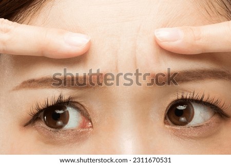 The woman points to the crease between her eyebrows. Royalty-Free Stock Photo #2311670531
