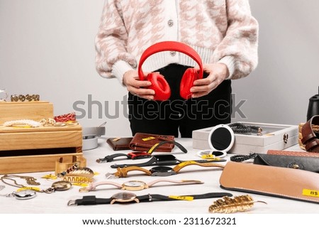 Woman holding headphones near table with different stuff indoors, closeup. Garage sale