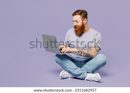 Full body young redhead bearded man wear violet t-shirt casual clothes sitting hold use work on laptop pc computer isolated on plain pastel light purple background studio portrait. Lifestyle concept