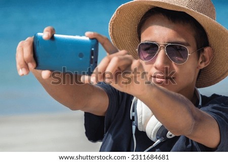 young man with hat and sunglasses making a selfie with phone on the beach