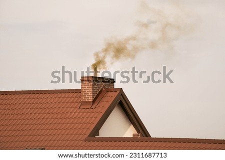 Black smoke comes out of a modern house chimney. The concept of global warming and environmental pollution. Heating with solid fuel. Royalty-Free Stock Photo #2311687713